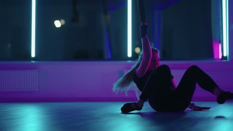 A-woman-does-yoga-and-stretching-on-a-hanging-hammock-in-neon-light.-A-woman-is-flying-in-a-hammock-in-the-studio-doing-stretching-and-body-exercises.-Exercises-in-the-air